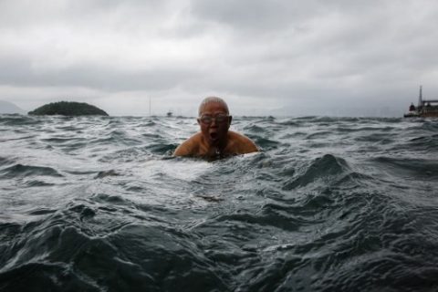 In this picture taken on June 2, 2017, Lau Sam-lan, 74, swims in front of a view of Kowloon (back) off the western tip of Hong Kong Island. Hong Kong's Victoria Harbour is one of the world's busiest ports, but every morning daring elderly swimmers dive in to its choppy waters against a teeming backdrop of ferries, cargo ships and fishing boats. / AFP PHOTO / Anthony WALLACE