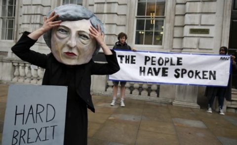 A demonstrator wears a mask depicting Britain's Prime Minister and leader of the Conservative Party Theresa May, poses with a mock gravestone bearing the words "Hard Brexit, RIP", during a protest photocall near the entrance 10 Downing Street in central London on June 9, 2017 as results from a snap general election show the Conservatives have lost their majority. British Prime Minister Theresa May faced pressure to resign on June 9 after losing her parliamentary majority, plunging the country into uncertainty as Brexit talks loom. The pound fell sharply amid fears the Conservative leader will be unable to form a government and could even be forced out of office after a troubled campaign overshadowed by two terror attacks. / AFP PHOTO / ADRIAN DENNIS