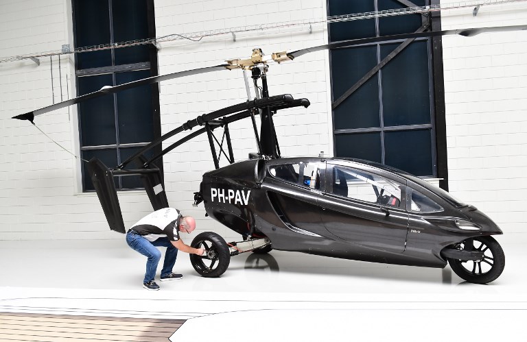 Chief Marketing Officer Markus Hess of the Dutch flying car developer PAL-V, poses next to one of the company's prototypes, at PAL-V's headquarter in Raamsdonksveer on May 30, 2017. After years of testing, a Dutch company is aiming to pip its competitors to the post, poised to start production of what they bill as a world first - a three-wheeled gyrocopter-type vehicle which will be certified for use on the roads and in the skies. The company, based in Ramsdonksveer just outside central Breda in The Netherlands, is aiming to deliver its first flying car by the end of 2018. / AFP PHOTO / EMMANUEL DUNAND