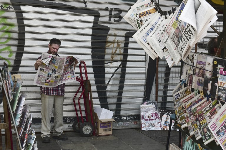 A man reads a newspaper next to a newspaper kiosk in central Athens on June 16, 2017. Eurozone ministers struck a long-delayed bailout deal with Greece on June 15, 2017 to unlock badly needed rescue cash, but warned Athens would have to wait for debt relief. / AFP PHOTO / LOUISA GOULIAMAKI