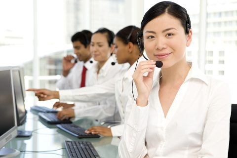 Portrait of a beautiful Chinese customer service representative at work with Multi-ethnic staff in the background.
