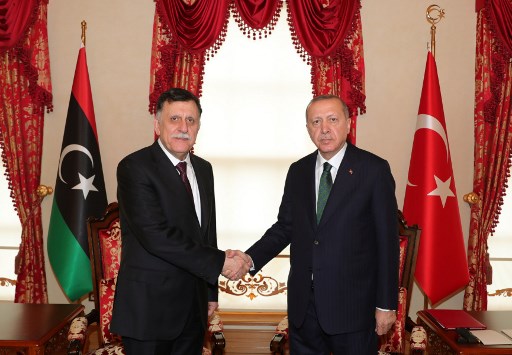 Two diplomats shaking hands in agreement between the Libya and Turkey flag